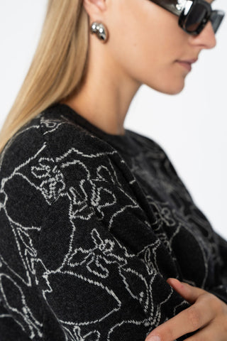 Close-up side profile of woman wearing dark grey knit merino wool sweater with floral design. 