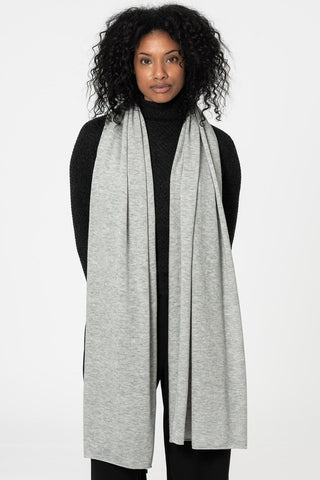 Woman standing in front of white background wearing black turtleneck sweater and light grey scarf. 