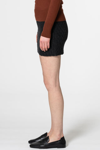 Side view of woman  in front of white background wearing brick mock neck sweater and onyx grey hand-crochet merino wool skirt by Dinadi. 
