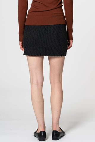 Back view of woman  in front of white background wearing brick mock neck sweater and onyx grey hand-crochet merino wool skirt by Dinadi. 