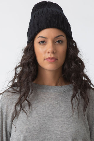 Woman in front of white background wearing black thick rib knit toque and grey fine knit sweater.