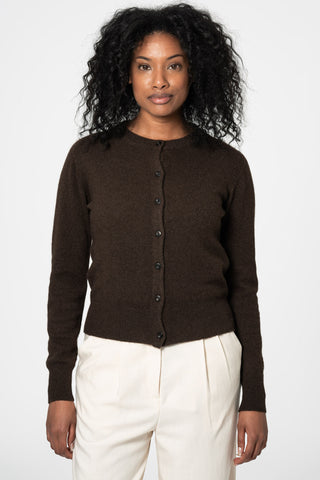 Woman in front of white background wearing dark brown yak wool knit cardigan by Dinadi paired with cream trousers. 