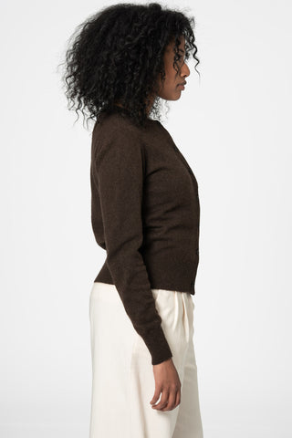Side view of woman in front of white background wearing dark brown yak wool knit cardigan by Dinadi paired with cream trousers. 