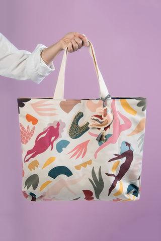 Beige with multi-colour abstract print tote bag being held in front of purple background. 