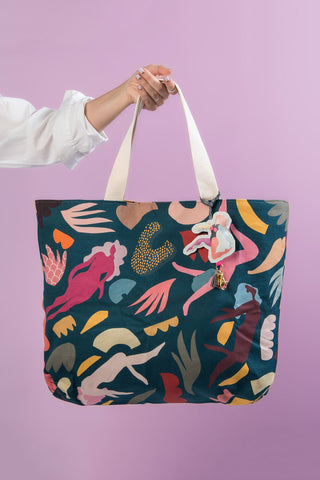 Teal blue tote abstract print tote bag being held in front of purple background. 