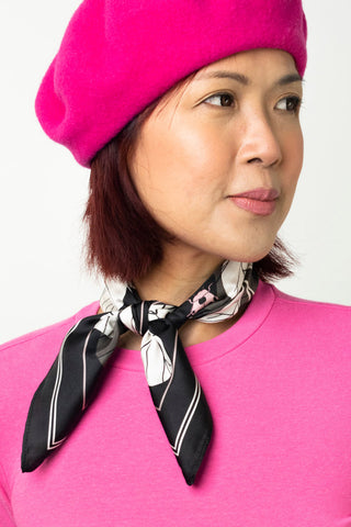 Woman with pink beret and shirt wearing black and white silk twill neckerchief tied around her neck. 