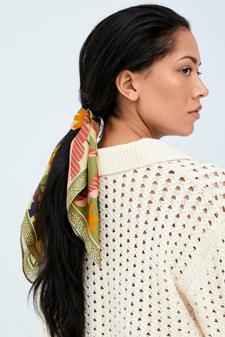 Woman in front of white background wearing green scarf tied around her hair. 