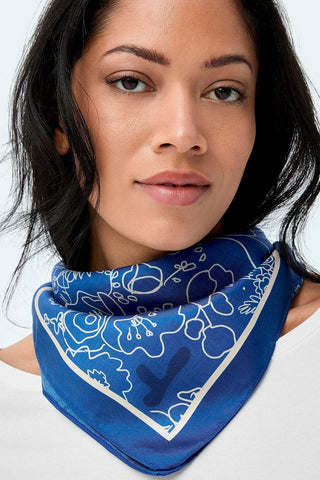 Woman wearing blue silk scarf with white floral illustration print. 
