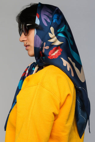 Woman wearing yellow sweater and dark blue & multi-colour printed scarf tied around her head. 