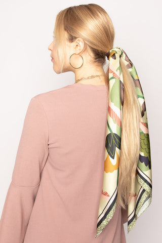 Back view of woman wearing pink long sleeve top and green and cream floral print scarf tied around her pony tail. 