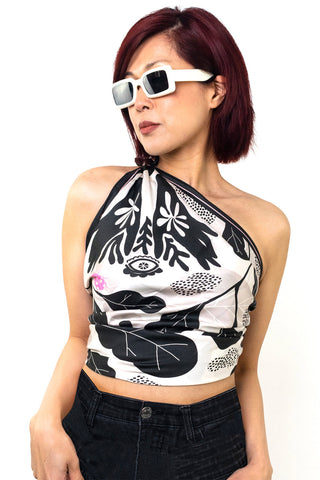 Woman in front of white background wearing black and white silk scarf worn as  a one shoulder top. 