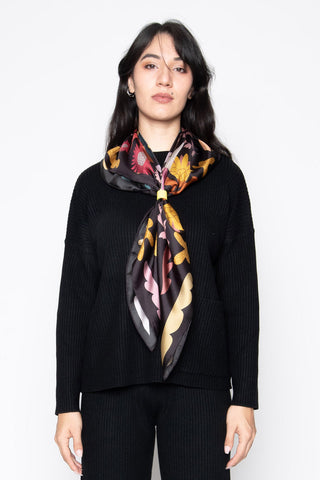 Woman wearing black scarf with multi-coloured abstract print tied around her neck. 
