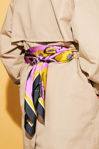 Close-up of person wearing tan trench coat with pink and black scarf tied like a belt in the back. 