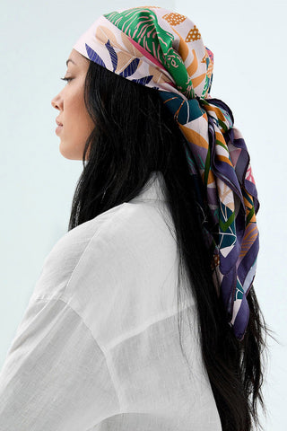 Woman wearing pink silk scarf with multi-colour print tied around her head. 