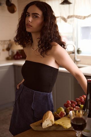 Woman standing in kitchen wearing black tube top and blue corduroy Cordelia skirt by Dorsali. 