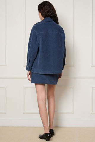 Back view of woman in front of white wall wearing matching denim blue corduroy Cordelia jacket and mini skirt by DorsaLi. 