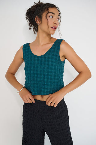 Woman wearing a teal seersucker top and black pants against a white background.