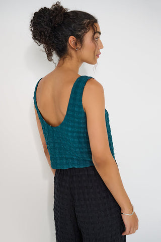 Back view of woman wearing a teal seersucker top and black pants against a white background.