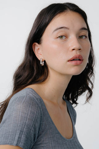 Close-up of model wearing grey t-shirt and sterling silver hoop earrings. 