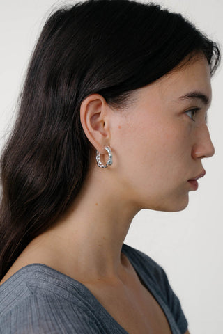 Side profile view of woman wearing grey t-shirt and sterling silver hoop earrings. 