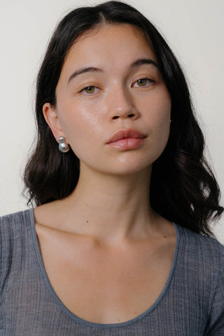 Woman wearing grey top with silver stud earrings. 