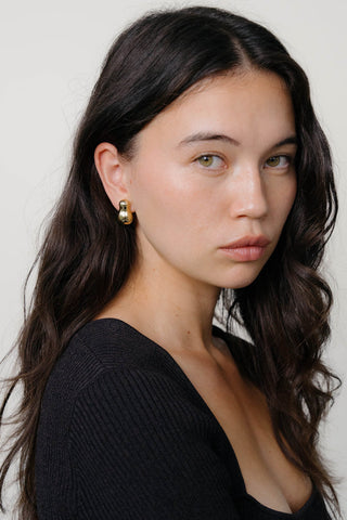 Woman wearing black top and gold stud earrings. 