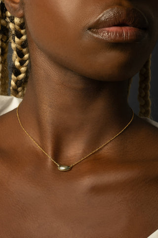Close-up of woman wearing gold chain with gold pebble pendant. 