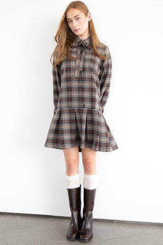 Woman in front of white wall wearing plaid babydoll Hope dress by Eve Lavoie, paired with brown boots and white socks. 