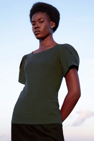 Woman standing in front of blue sky wearing dark green short sleeve blouse with tulip style sleeves. 