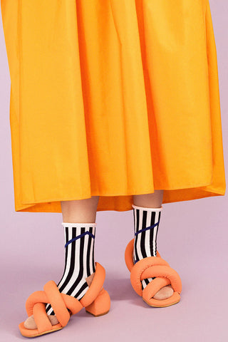 Close-up of women's legs wearing orange dress, orange shoes and black and white Chelsea rolled top crew sock by Hansel from Basel. 
