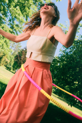 Jennifer Glasgow wearing beige cropped top with coral pleated midi skirt. 