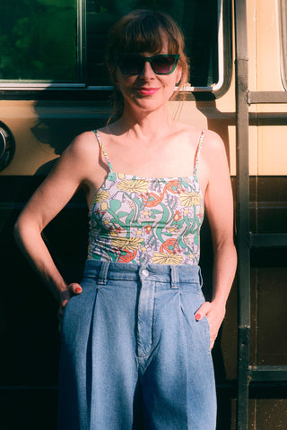 Woman in front of vintage van wearing floral printed tank with pleated denim pants.