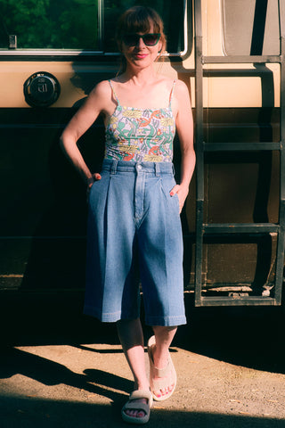 Woman in a floral printed tank and wide leg knee length denim shorts standing in front of a vintage van.