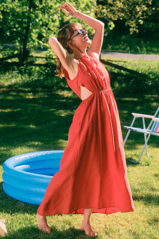Woman in garden with kiddy pool in background, wearing red maxi dress with side cut-outs.  