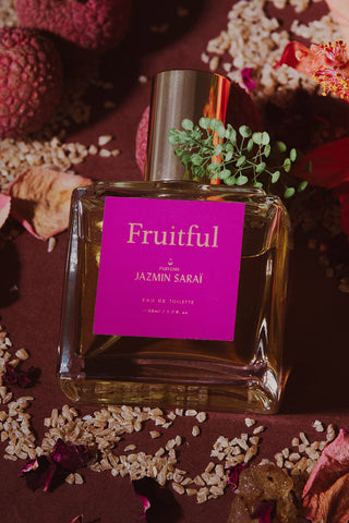 Perfume bottle labeled 'Fruitful' by Jazmin Sarai on a decorative background with flowers and seeds.