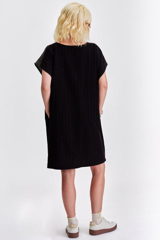 Back view of woman in front of  white background wearing black relaxed fit tunic. 