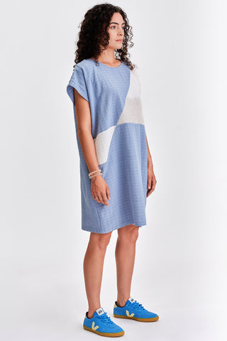 Woman in front of  white background wearing light blue and white colour blocked relaxed fit tunic. 