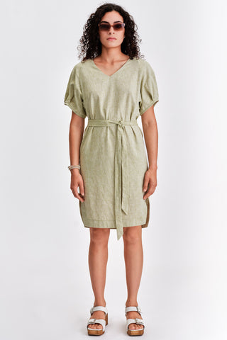 Woman in front of white background wearing light green belted v-neck dress with white sandals. 