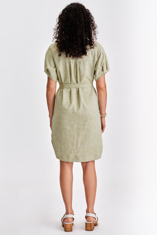 Back view of woman in front of white background wearing light green belted v-neck dress with white sandals. 