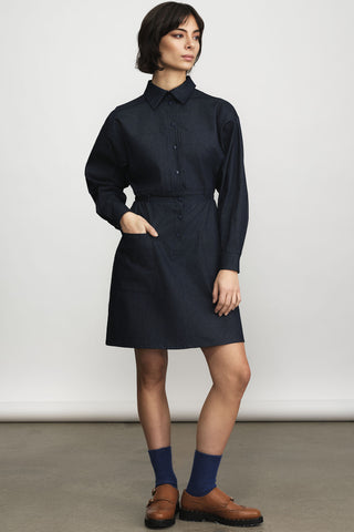 A model wearing a dark navy blue long-sleeve shirt dress with a button-down front and collar, styled with navy socks and brown leather loafers against a neutral studio background.