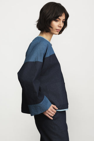 A side view of a woman wearing a denim colour-blocked jacket in front of a plain light gray background.