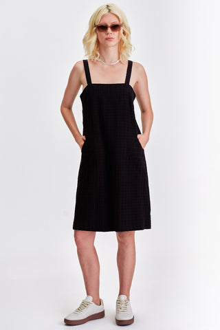 Woman in front of white background wearing black knee length summer dress. 