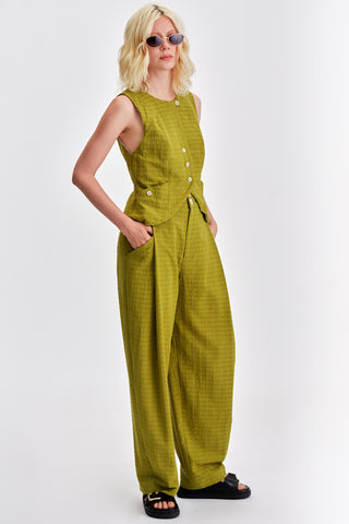 Woman in front of white background wearing  matching green button up shirt and pleat front pants. 