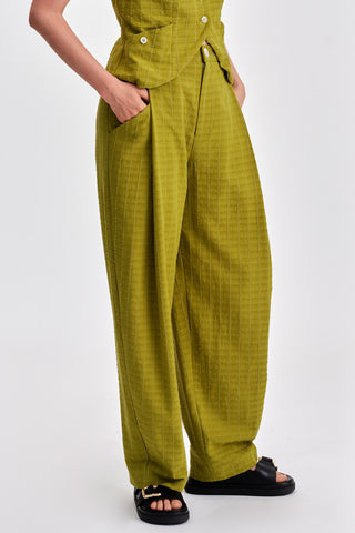 Woman in front of white background wearing green pleat front pants. 