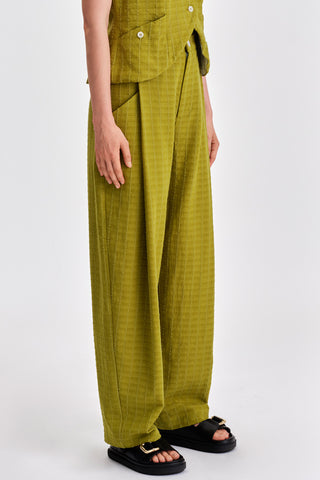 Woman in front of white background wearing green pleat front pants. 