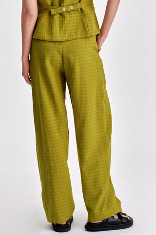 Back view ofwoman in front of white background wearing green pleat front pants. 