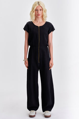 Woman in front of white background wearing short sleeve jumpsuit with brass front zipper and elastic waist. 