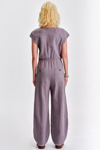 Back view of woman in front of white background wearing grey short sleeve jumpsuit with elastic waist. 