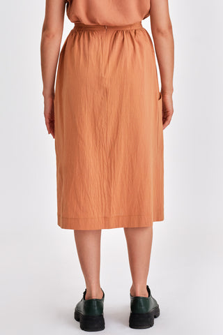 Back view of woman in front of white background wearing caramel orange voluminous midi length skirt and green leather lace-up shoes. 