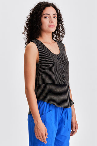 Woman wearing a black striped tank top and blue pants in front of a white background